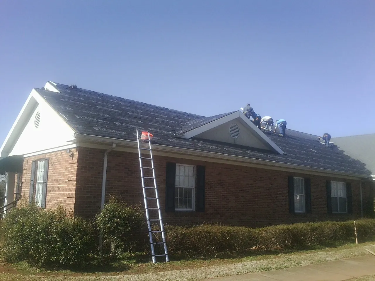Crew tearing shingles off a brick ranch roof with a ladder set — Metal Roof Repair work by our crew in Newton Center