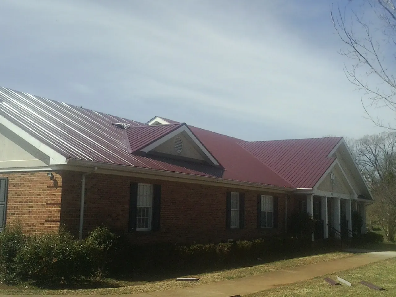 Red metal roof with gabled entries on a long brick building, from a Hail Damage Roof Repair job in Newton Center
