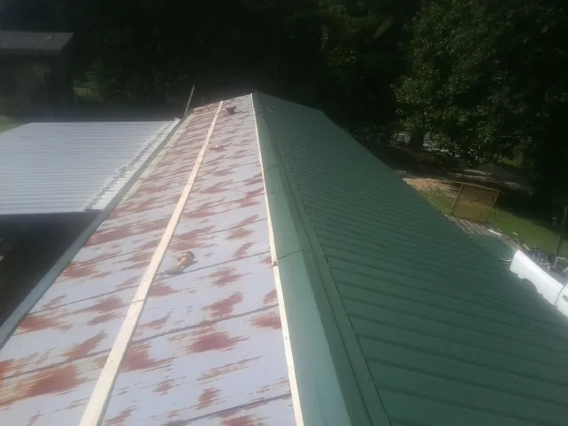 Old rusted panels beside newly installed green metal roofing — Wind Damage Roof Repair by Roofing Brothers in Newton Center