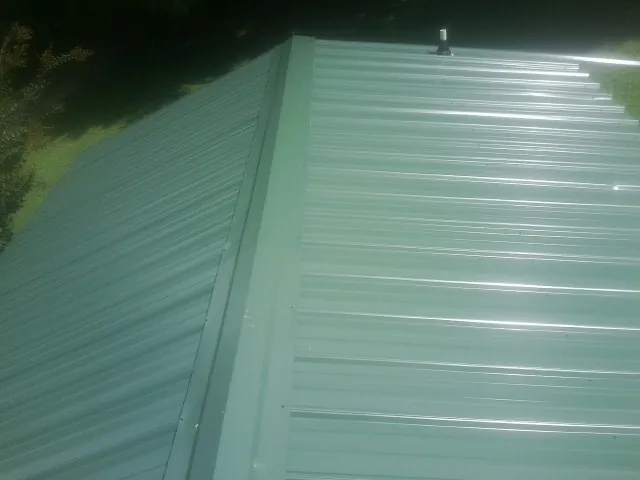 New green metal panels meeting at the ridge of a roof — Flat Roof Repair work by our crew in Newton Center