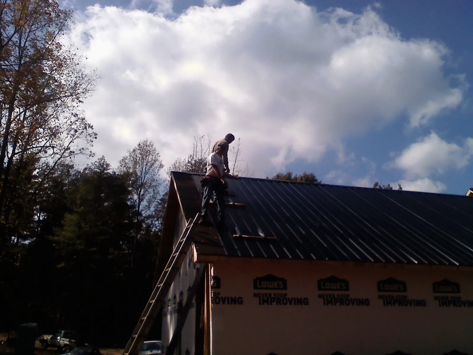 Roofer fastening dark metal panels high against a cloudy sky, from a Roof Inspection job in Newton Center