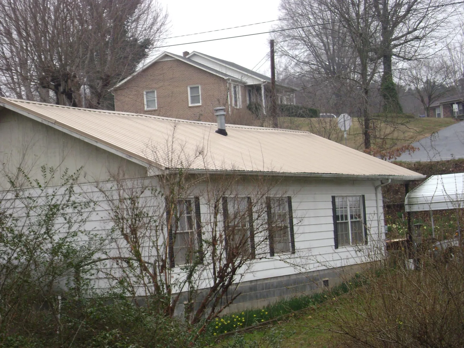 Tan metal roof on a white sided house set into a hillside — Commercial Roofing by Roofing Brothers in Newton Center