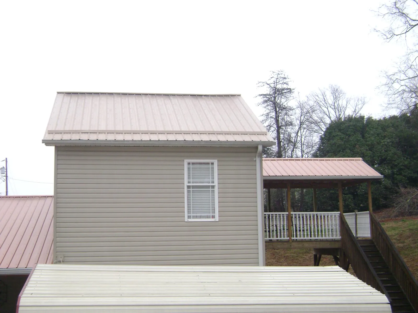 Tan metal roofs on a two story addition and attached porch, from a Roof Replacement job in Newton Center